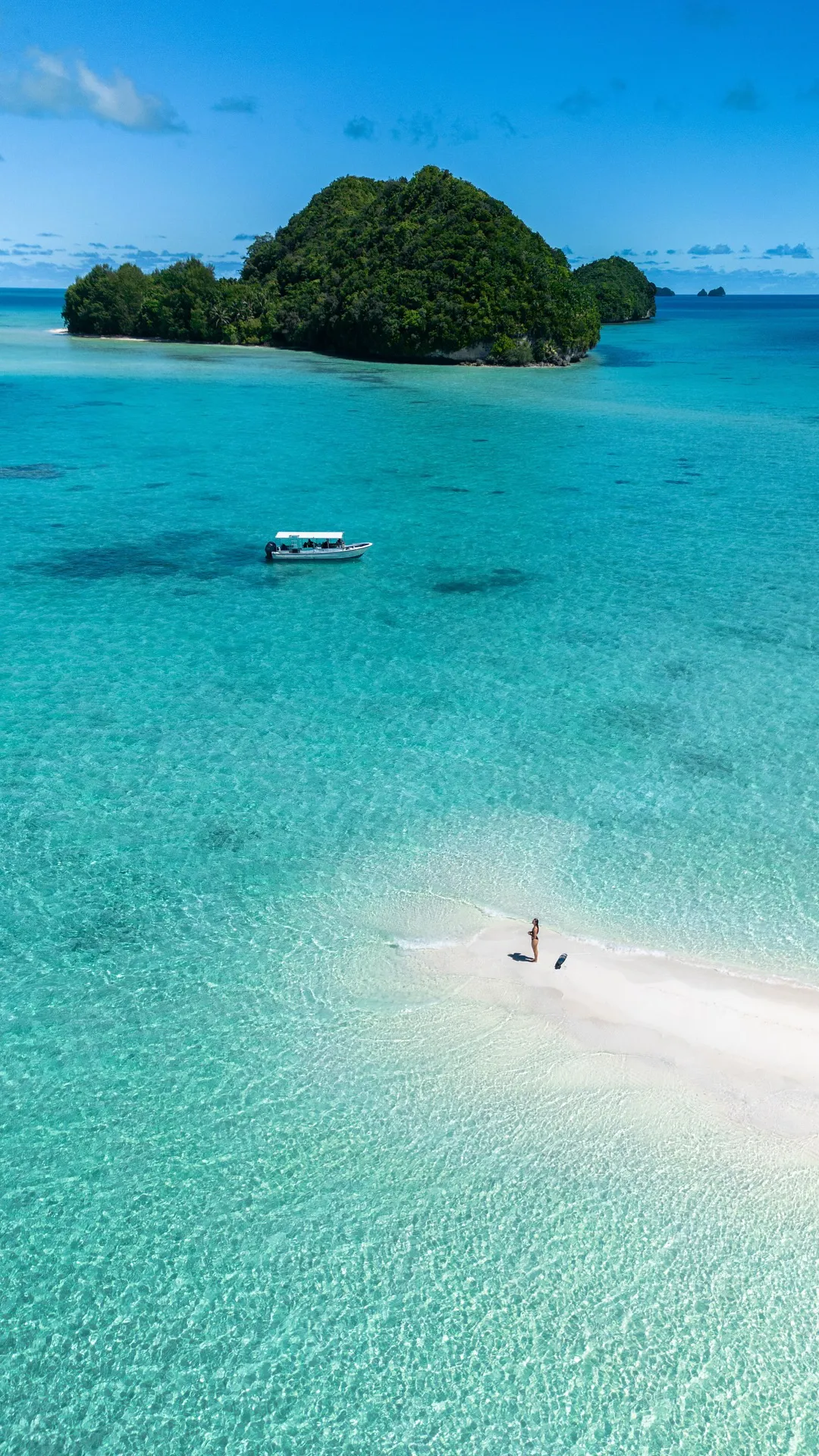 aerial photo of turquoise waters, a sandy strip with a person and a pristine island in the back ground in tropical Palau