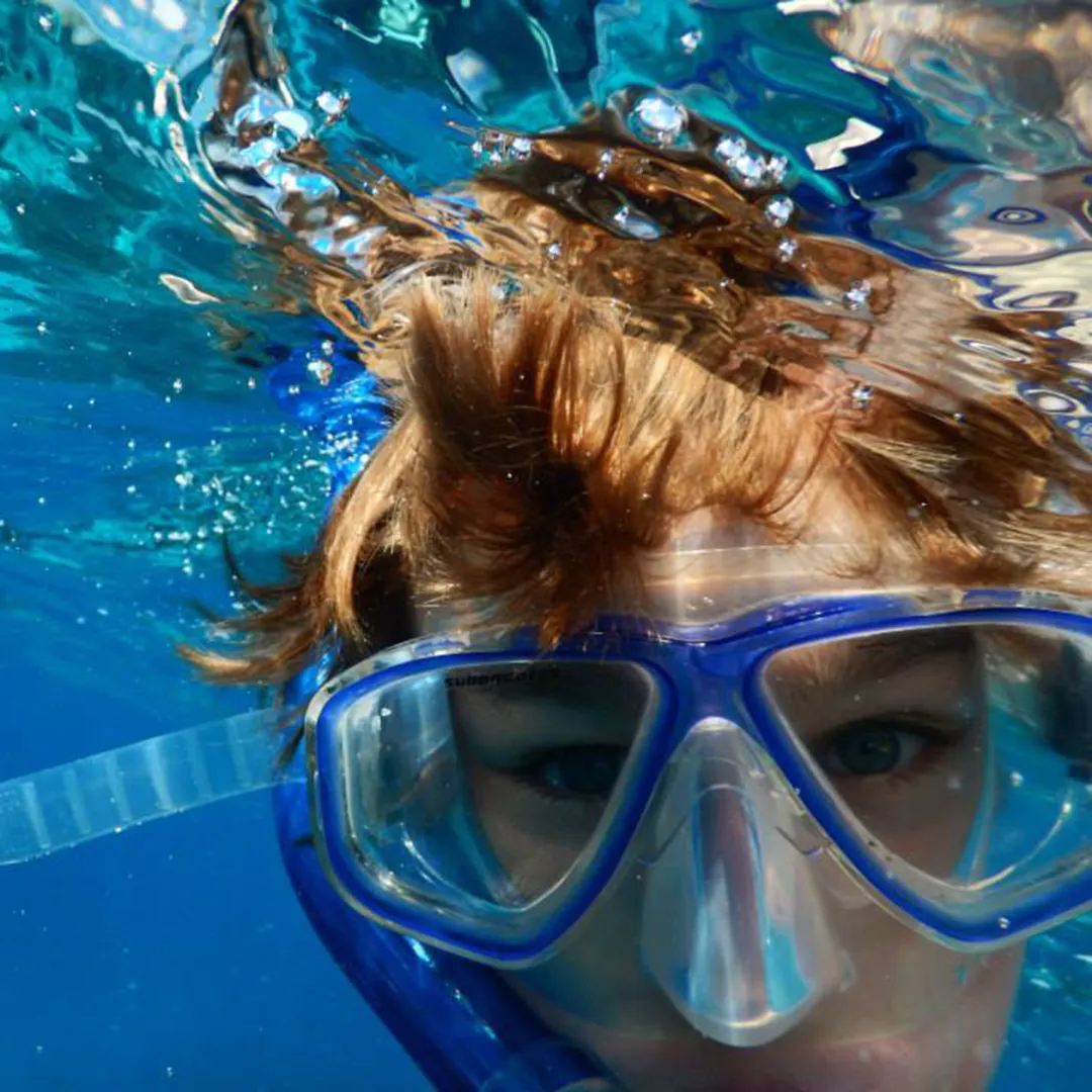 underwater photo of a snorkeler close up looking into the camera, just upper head and eyes behind mask visible