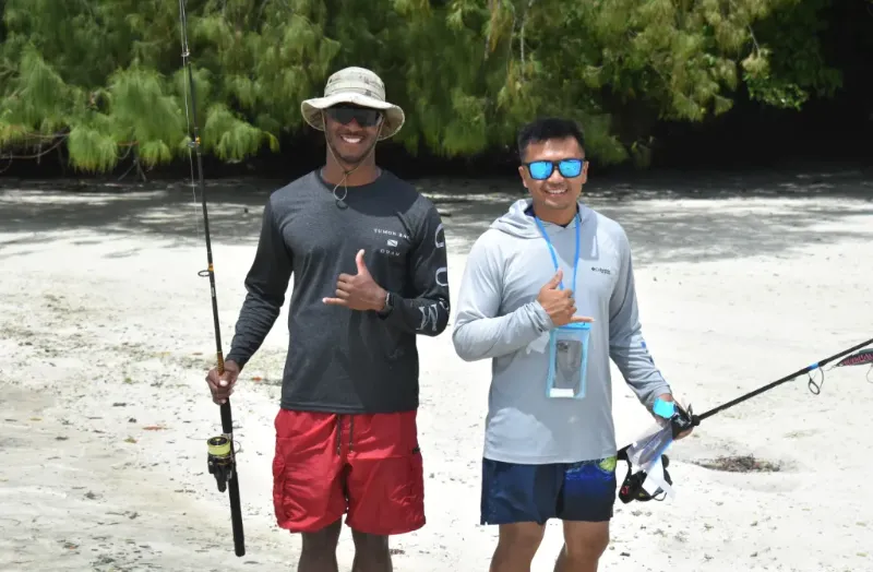 2 guys with fishing routes at the beach giving okay sign to the camera