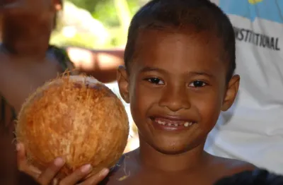 Palauan boy offering a coconut drink to the photographer